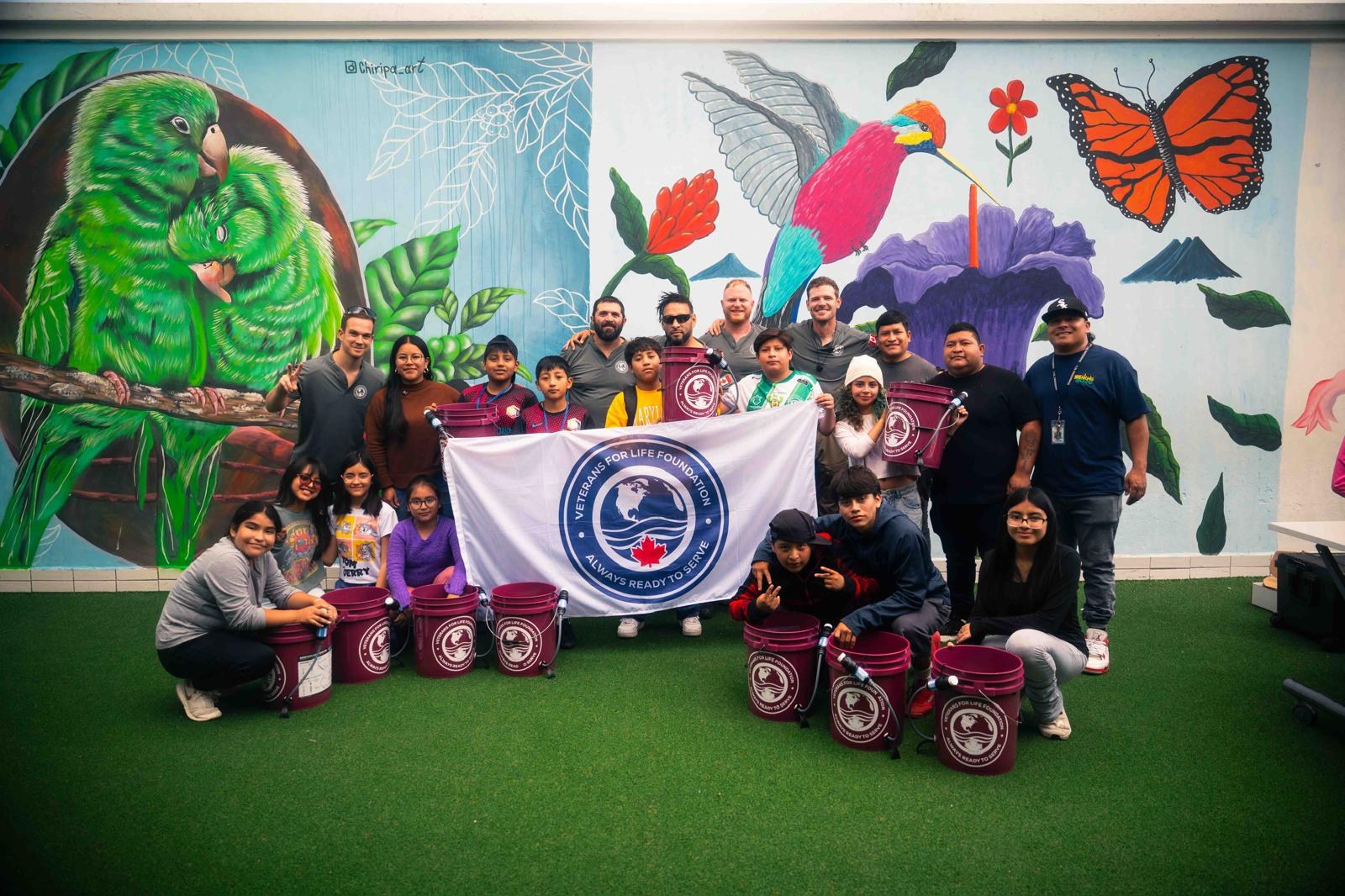 L’équipe de V4LF et des jeunes devant une murale, avec le drapeau de V4LF et des seaux de filtration